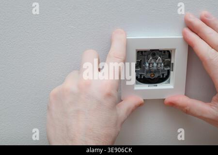 Un électricien remplace un interrupteur mural. Un concept de projet DIY. Danger de haute tension. Électricien réparant le panneau de commande de l'éclairage mural. Banque D'Images