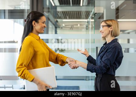 Deux femmes d'affaires diverses se serrant la main dans un bureau moderne, signifiant un partenariat réussi, un accord, une introduction et un accueil professionnel lors d'une réunion Banque D'Images