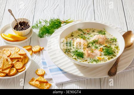 Un bol de lohikeitto nordique traditionnel ou soupe crémeuse de saumon laxsoppa avec des morceaux de poisson et de l'aneth frais servi avec des craquelins, des tranches de citron et du poivre Banque D'Images