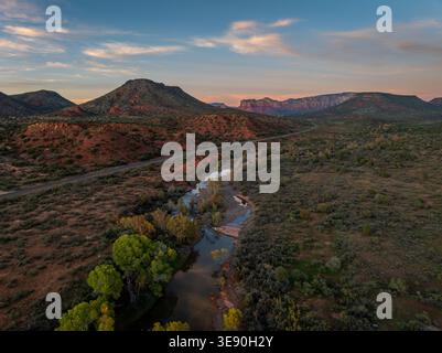 Vue aérienne de la rivière sinueuse et de la route à travers le canyon de roche rouge avec des arbres verdoyants au coucher du soleil près de Sedona Arizona. Banque D'Images