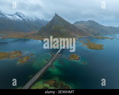 Vue aérienne des ponts de Fredvang couvrant l'eau turquoise vers un pic de montagne abrupt sous un ciel nuageux à Fredvang, Nordland, Norvège. Banque D'Images