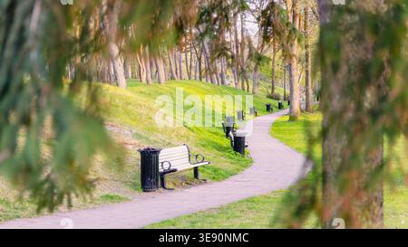 Mouvement doux à travers l'espace dans le sentier sinueux avec des bancs et des pentes vertes dans le parc Liepaja, la lumière du printemps tôt crée une direction calme et l'urb ouvert Banque D'Images