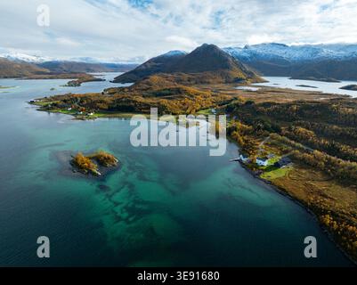 Vue aérienne de Hamn i Senja avec des eaux côtières turquoises, feuillage d'automne vibrant sur les collines, et montagnes lointaines enneigées à Skaland, Tro Banque D'Images