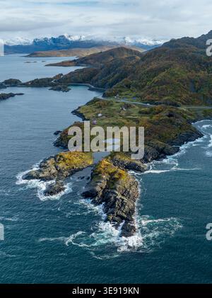 Vue aérienne de Hamn i Senja avec falaises rocheuses escarpées, routes côtières sinueuses et montagnes enneigées sous un ciel nuageux à Skaland, Troms, Norw Banque D'Images