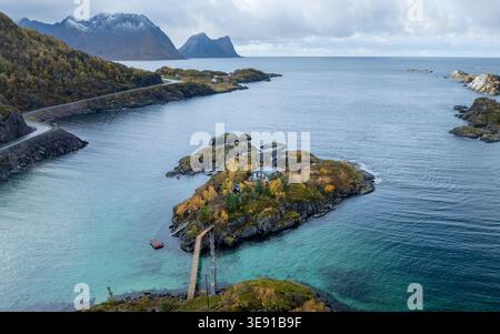 Vue aérienne de la station Hamn i Senja sur une île rocheuse avec feuillage d'automne et eau turquoise contre des montagnes enneigées à Skaland, Troms, Norvège. Banque D'Images
