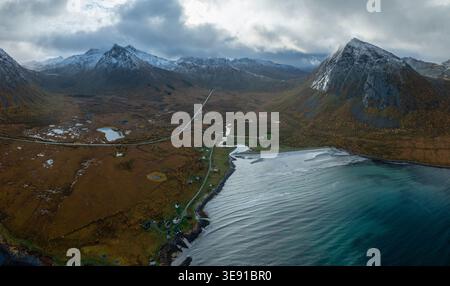 Vue aérienne de la baie de Ballesvika avec son eau turquoise, route côtière sinueuse et montagnes enneigées sous un ciel nuageux à Ballesvika, Troms, Norwa Banque D'Images