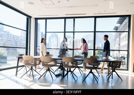 Professionnels confiants se serrant la main près de l'équipe dans la salle de conseil au bureau pendant la journée Banque D'Images