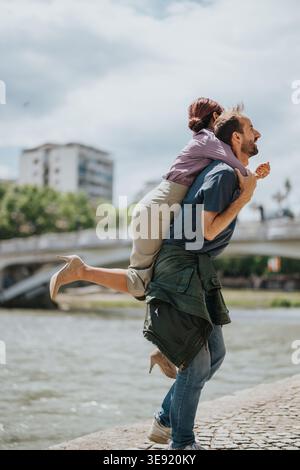 Collègues d'affaires appréciant un piggyback ludique au bord de la rivière lors d'une sortie urbaine décontractée Banque D'Images