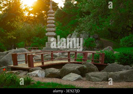 Une scène paisible de jardin japonais avec un pont en bois courbé, une grande pagode en pierre et de grands rochers entourés de verdure vibrante et d'arbres, avec Banque D'Images