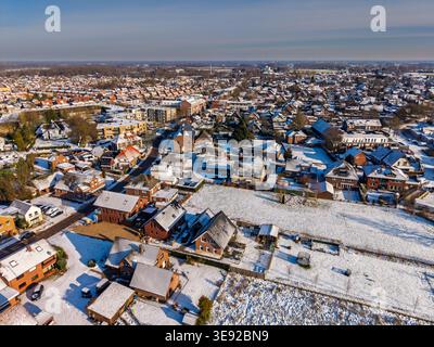 Vue aérienne d'un village européen enneigé sous un ciel bleu clair. Les maisons en briques aux toits enneigés sont regroupées autour d'une église et de champs ouverts. A Banque D'Images