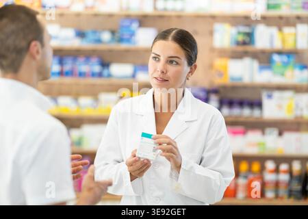 Femme consultant pharmacien tient la boîte dans les mains et offre le client homme pour acheter remède Banque D'Images