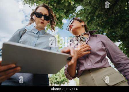 Des collègues examinent une tablette ensemble à l'extérieur lors d'une réunion informelle sous les arbres Banque D'Images