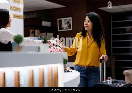 Le préposé à la réception remet la carte-clé asiatique une fois l'enregistrement terminé. Après avoir terminé le processus de réservation pour l'hôtel agréable, le client est prêt à aller à l'hébergement. Banque D'Images