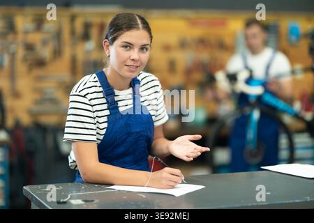 Mécanicien féminin amical remplissant des formulaires de service dans un atelier de réparation de vélos Banque D'Images