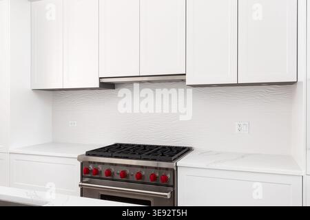Détail de cuisine moderne avec une cuisinière à gaz élégante et des meubles blancs élégants avec un dosseret en tuiles ondulées. Banque D'Images