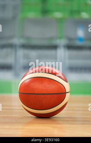 Ballon de basket-ball assis sur un sol de gymnase en bois poli. Reflétant les lumières et le fond flou du lieu sportif Banque D'Images