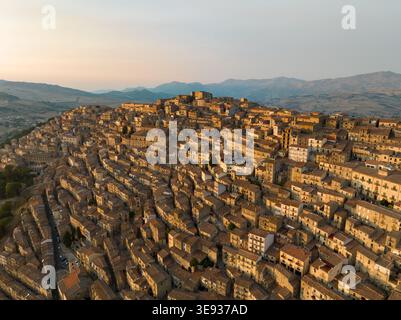 Vue aérienne de la ville historique perchée de Gangi avec ses maisons en pierre serrées sur une pente raide pendant l'heure dorée à Gangi, Sicile, Italie. Banque D'Images