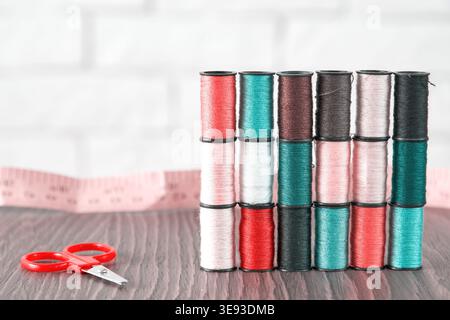 Bobines de fil à coudre multicolores, ciseaux et ruban à mesurer sur une table en bois. Fournitures de confection professionnelle pour la mode et l'artisanat de bricolage Banque D'Images