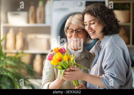 Moment de vie réconfortant d'une mère âgée et sa fille adulte partageant une étreinte joyeuse et admirant un bouquet vibrant de tulipes. L'image Banque D'Images