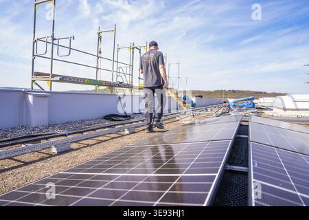 Personne travaillant entre les panneaux solaires sur un toit sous un ciel dégagé, assemblage PV. OBI Baumarkt, Muehlacker, Enzkreis, Allemagne Banque D'Images
