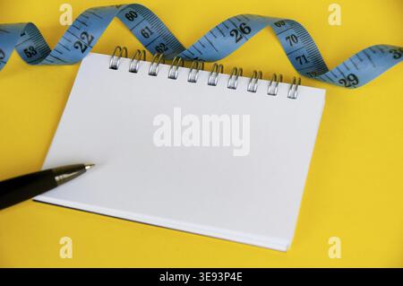 Ruban de mesure diététique avec cahier vierge sur couverture jaune Banque D'Images