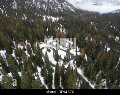 Vue aérienne de la route sinueuse de Passo Giau serpentant à travers une dense forêt de pins enneigée dans les Dolomites Cortina d'Ampezzo, Vénétie, Banque D'Images