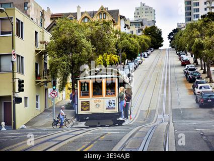 Un téléphérique monte dans une rue escarpée de San Francisco. Les gens regardent depuis les trottoirs les voitures se garer le long de la route. Banque D'Images