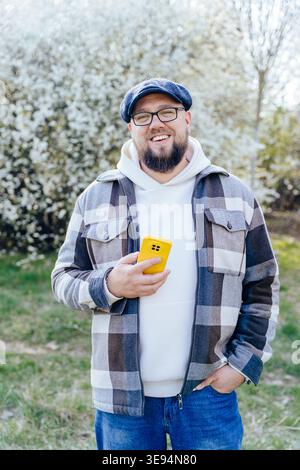 Portrait vertical d'un homme caucasien barbu souriant en surpoids tenant un smartphone jaune Banque D'Images
