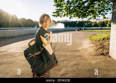Femme souriante 40 avec sac à dos portant baguette dans le parc Banque D'Images