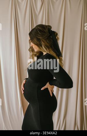 Femme enceinte en robe noire posant de profil par fond beige Banque D'Images
