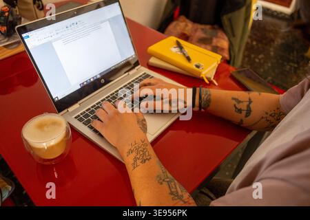 Gros plan des mains tatouées tapant sur le clavier d'ordinateur portable pour indépendant créatif et concept alternatif de travail à distance Banque D'Images