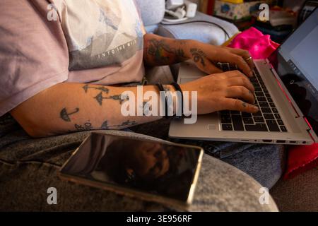 Gros plan des mains tatouées tapant sur le clavier d'ordinateur portable pour indépendant créatif et concept alternatif de travail à distance Banque D'Images
