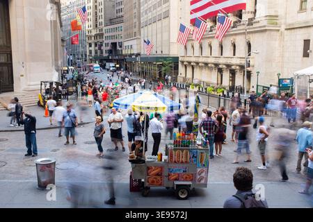 Une scène de rue animée à New York avec des gens marchant et un chariot de nourriture sous un parapluie bleu et jaune. Banque D'Images