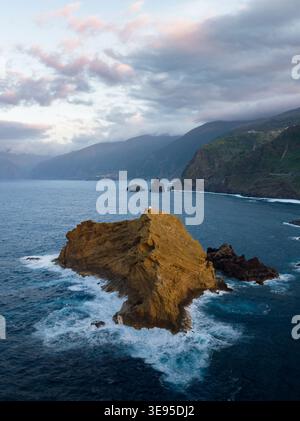 Vue aérienne de la formation rocheuse Ilheu mole avec un petit phare entouré de vagues et de falaises côtières abruptes Porto Moniz, Madère, Portugal. Banque D'Images