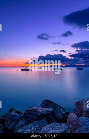 Coucher de soleil serein sur le lac de Garde avec des bateaux et Rocky Shore Banque D'Images