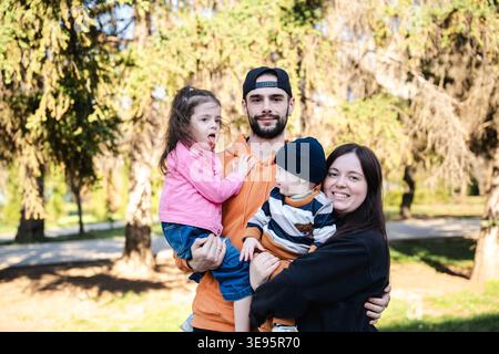 Famille avec père mère et deux enfants debout dans le parc tenant les enfants et regardant la caméra avec des expressions chaudes. Concept de lien familial et PA Banque D'Images