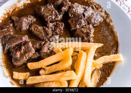 Cubes de bœuf cuits dans une sauce brune riche servis avec des frites dorées sur une assiette - plat principal copieux et réconfortant prêt à manger Banque D'Images