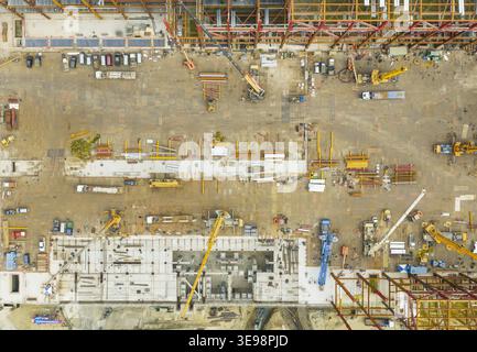 Vue aérienne d'un grand chantier de construction industrielle avec charpentes en acier, grues jaunes et machinerie lourde sur un sol en terre battue à Taiwan. Banque D'Images