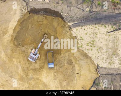 Vue aérienne d'une excavatrice creusant dans une grande fosse à terre à côté d'un camion à benne basculante bleu sur un chantier de construction à Taiwan. Banque D'Images