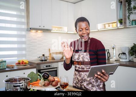 Femme cuisinant et ayant un appel vidéo sur tablette numérique Banque D'Images
