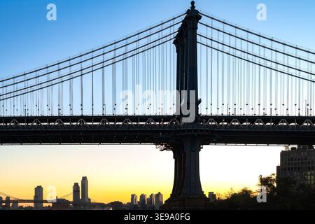 La silhouette du pont de Manhattan se dresse contre la lueur vibrante de l'horizon au petit matin. Banque D'Images