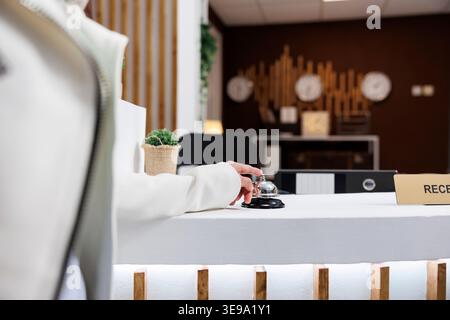 Femme sonnant la cloche de la réception attendant d'obtenir un soutien pendant le séjour à la station moderne. La réception est vide et les clients de l'hôtel cherchent à obtenir le service de la réceptionniste pendant leurs vacances Banque D'Images