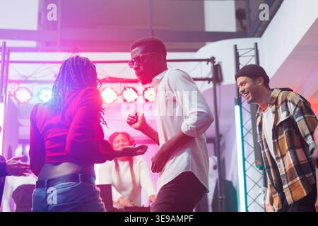 Danseurs afro-américains couple improvisant des mouvements dans la discothèque de musique électronique en direct dans la boîte de nuit. Énergique jeune homme et femme dansant et faisant la fête sur dancefloor en club Banque D'Images