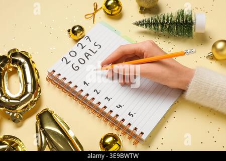 Femme avec la figure 2026 et décor de Noël écrivant la liste à faire sur fond jaune Banque D'Images