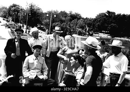 Historique 1956 vue d'archives de Slavyanogorsk (aujourd'hui Sviatohirsk) présentant un rassemblement animé en plein air de personnes âgées. La scène capture un groupe d'hommes et de femmes vêtus de façon décontractée souriant et conversant sur une terrasse pavée avec une balustrade, tandis qu'un homme joue d'un accordéon traditionnel. Ce moment nostalgique du milieu du XXe siècle met en évidence la culture sociale dynamique, les traditions musicales et les loisirs communautaires de l'ère soviétique, préservant la vie quotidienne historique et les habitants de la région, reflétant le Donbass paisible. Banque D'Images