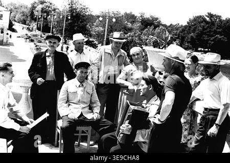Historique 1956 vue d'archives de Slavyanogorsk (aujourd'hui Sviatohirsk) présentant un rassemblement animé en plein air de personnes âgées. La scène capture un groupe d'hommes et de femmes vêtus de façon décontractée souriant et conversant sur une terrasse pavée avec une balustrade, tandis qu'un homme joue d'un accordéon traditionnel. Ce moment nostalgique du milieu du XXe siècle met en évidence la culture sociale dynamique, les traditions musicales et les loisirs communautaires de l'ère soviétique, préservant la vie quotidienne historique et les habitants de la région, reflétant le Donbass paisible. Banque D'Images