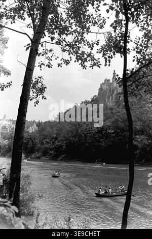 Historique 1956 vue d'archives de Slavyanogorsk (aujourd'hui Sviatohirsk) montrant la pittoresque rivière Siverskyi Donets encadrée par des silhouettes d'arbres sombres. La scène capture de petites barques et un tramway fluvial naviguant sur l'eau, avec la majestueuse église de craie de tous Nicholas s'élevant sur la falaise en arrière-plan. Ce paysage nostalgique du milieu du XXe siècle met en valeur la beauté naturelle et le patrimoine architectural de l'ère soviétique, préservant l'environnement historique de la région, reflétant le Donbass paisible. Banque D'Images