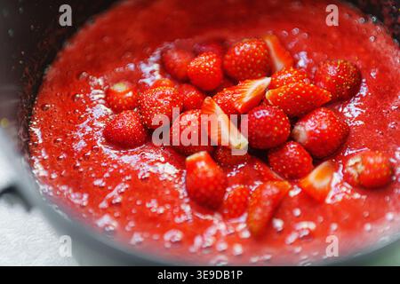 Un pot sur un poêle avec de la confiture de fraises bouillonnante étant remuée avec une cuillère. Concept de confiture de fraises maison. Banque D'Images