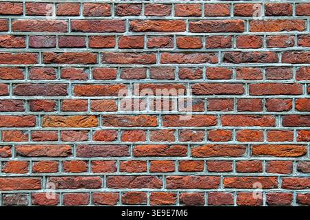 Beau mur de briques multicolore avec des tons rouges et oranges variés au foyer sélectif. La texture détaillée et les joints de mortier soulignent le motif historique. Banque D'Images