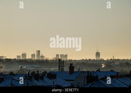 La ligne d'horizon lointaine des gratte-ciel dans le centre de Manchester vue au-dessus des toits enneigés des maisons, Bury, Greater Manchester. Banque D'Images